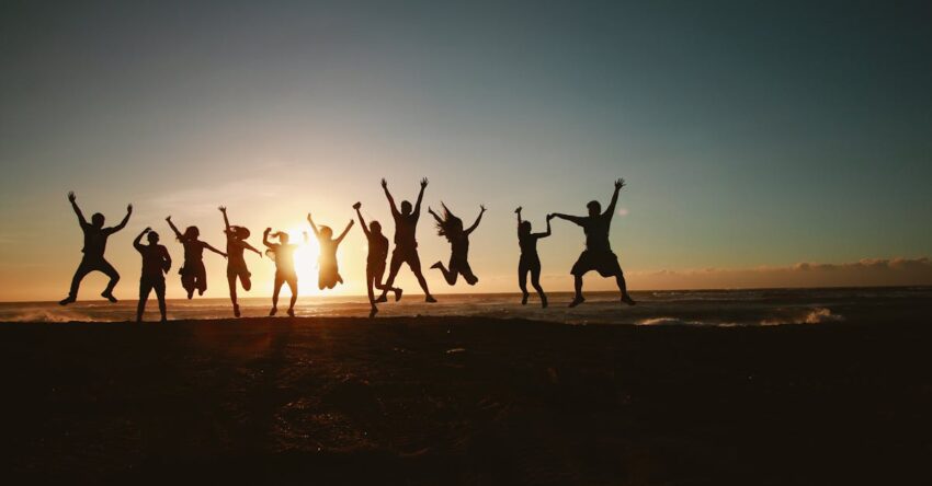 Silhouette of a group of friends jumping on a beach at sunset, expressing joy and freedom.