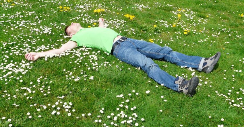 A man lies peacefully in a flowered meadow, embodying relaxation and summer joy.