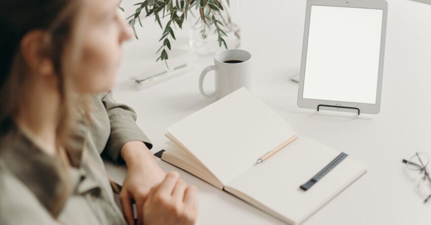 Woman sitting at a desk with blank tablet and notebook in a modern home office setting.