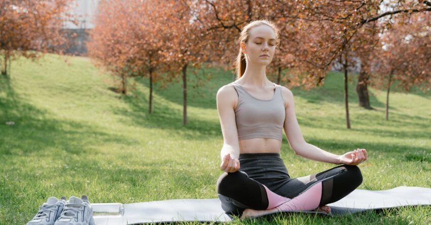 A woman practicing meditation on a yoga mat in a tranquil park setting during springtime.