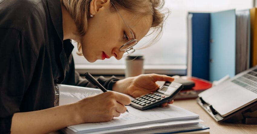Young woman diligently working on accounting with a calculator and documents. Perfect for business and finance themes.